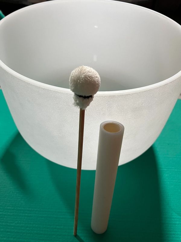A white crystal singing bowl with a mallet and a cylindrical case on a teal surface.