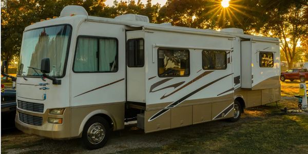 White and beige RV parked at sunset with extended slide-outs.