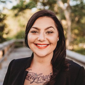 Smiling woman with dark hair and tattoo.
