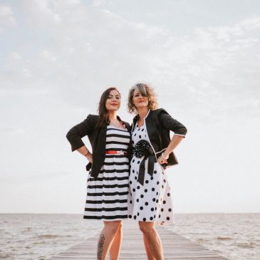 Two confident women posing on a dock by the sea.