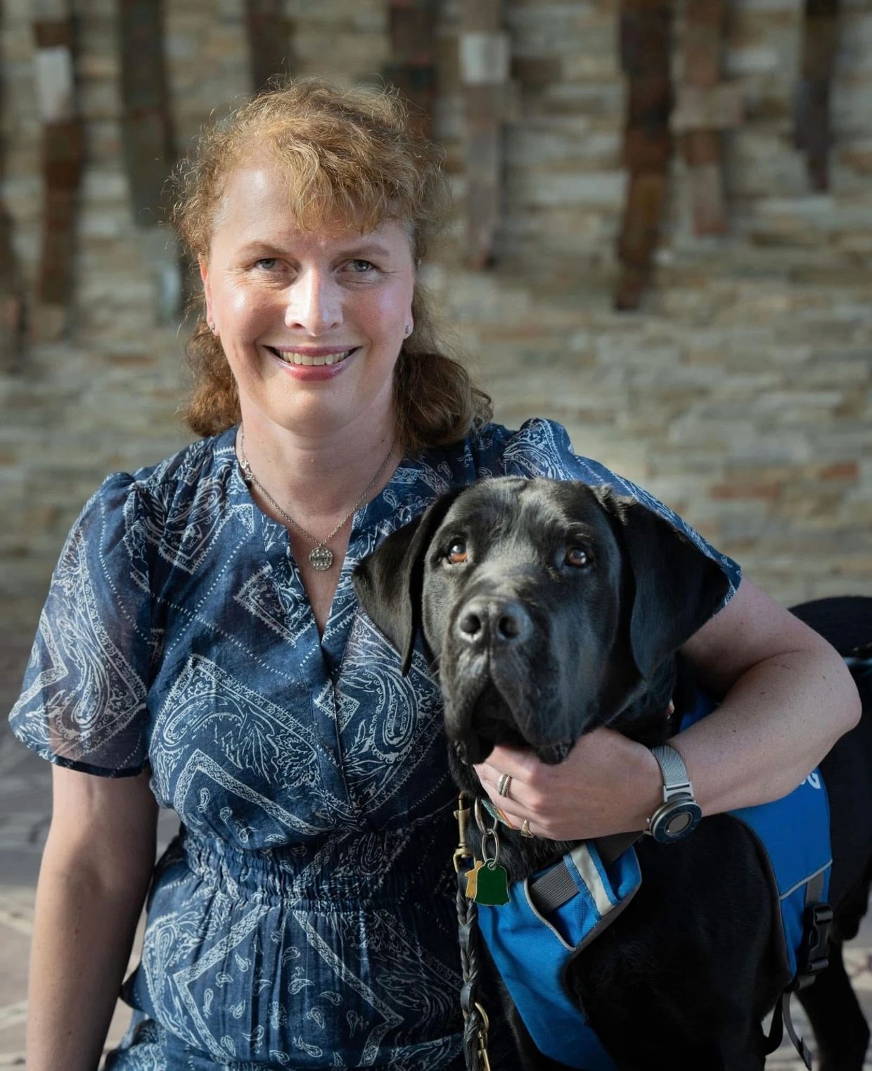 Kathy posing in a blue dress with her guide dog , Tate.