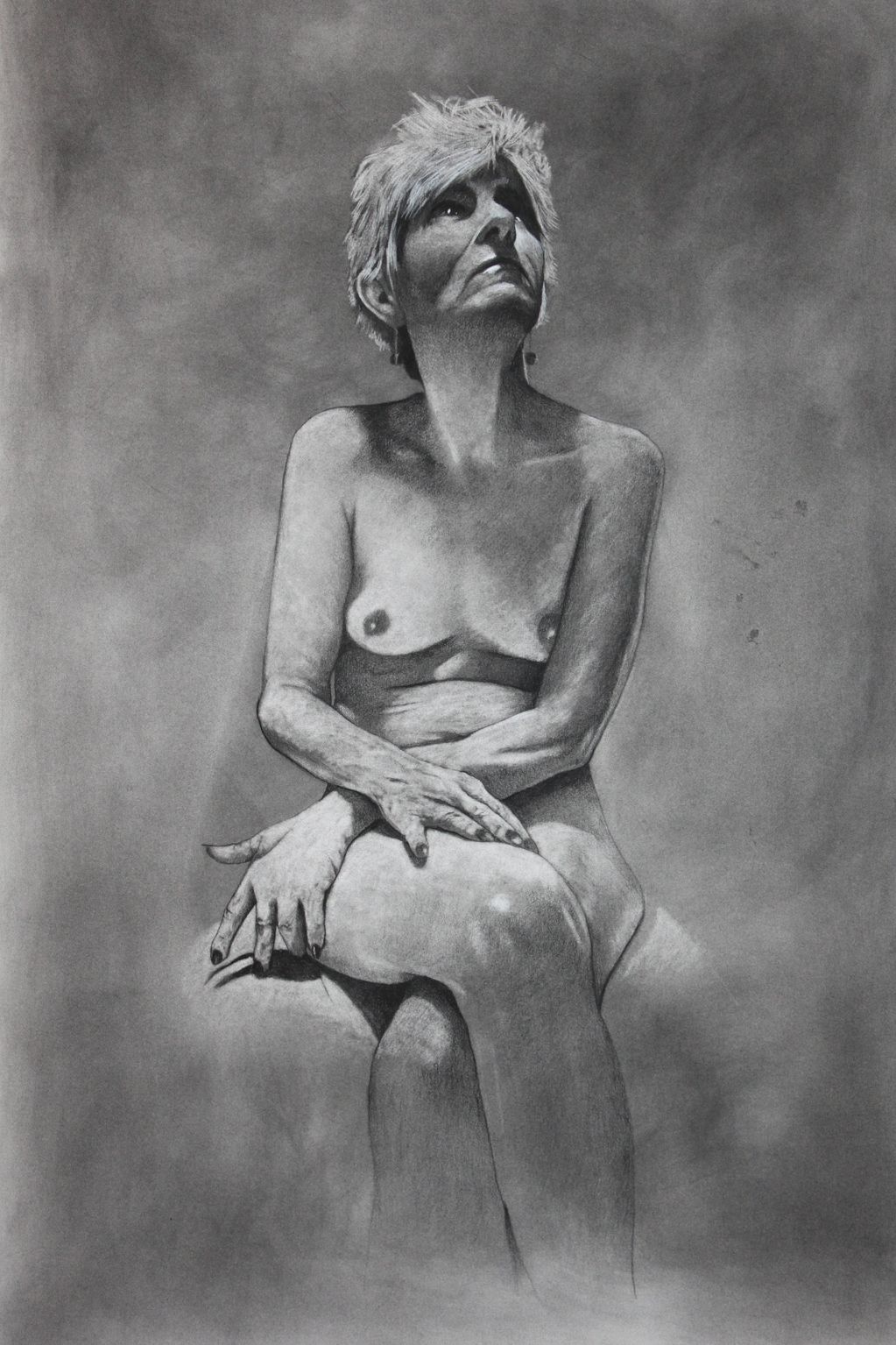Charcoal drawing of a seated nude woman with short hair, gazing upwards.