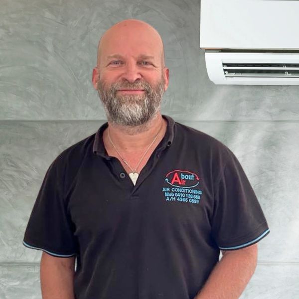 Nigel, owner of About Air pictured in blue polo neck shirt, next to an air conditioning unit