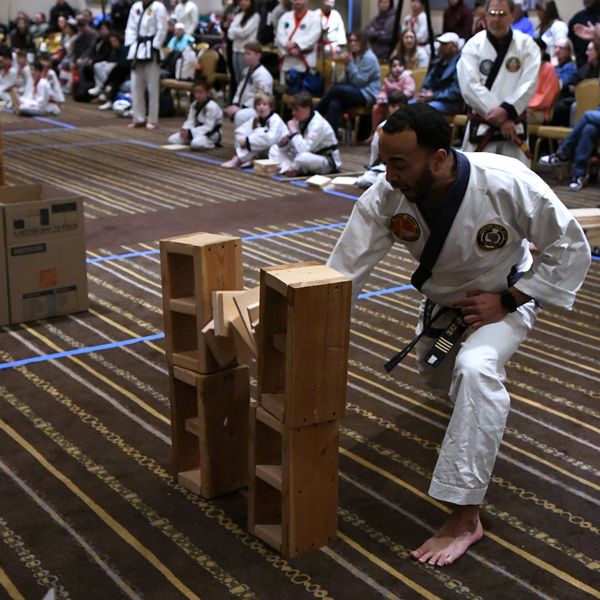 Martial artist breaking wooden boards during a demonstration with an audience.