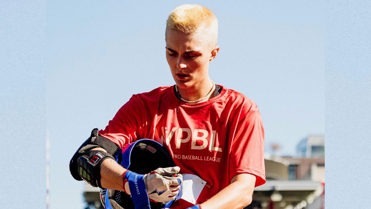 Young baseball player in red WPBL shirt holding helmet and gloves.