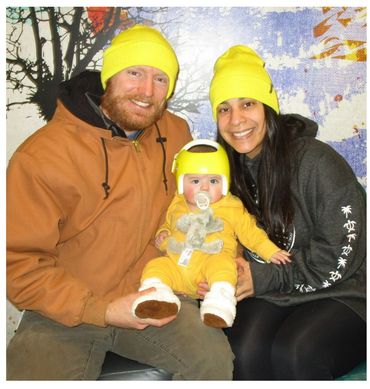 Two parents wearing bright yellow hats with their baby wearing a bright yellow starband.
