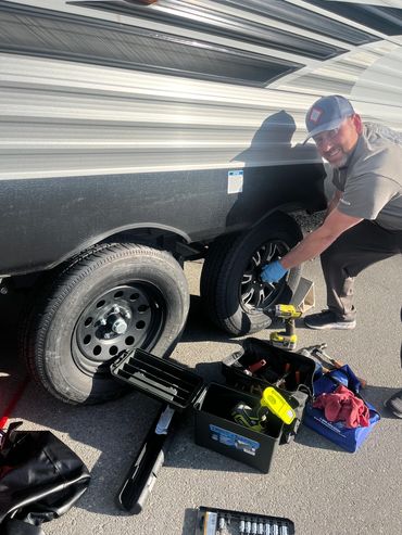 Man changing a tire on a trailer with tools scattered around.