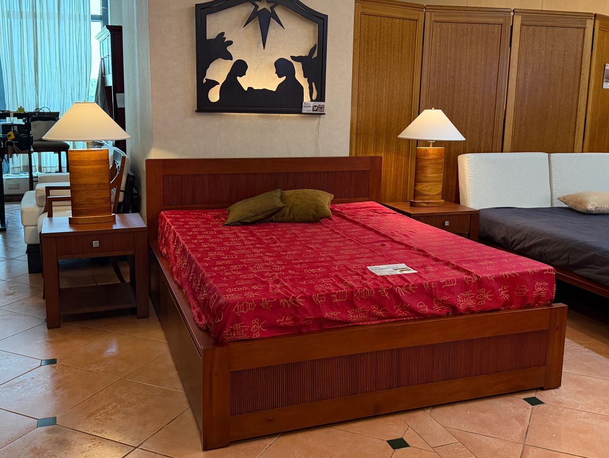 A bedroom with a wooden bed, red bedspread, two lamps, and nativity wall art.