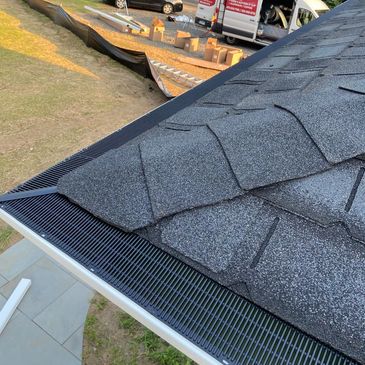 Newly installed gutter guard on a roof with construction materials and vehicles below.