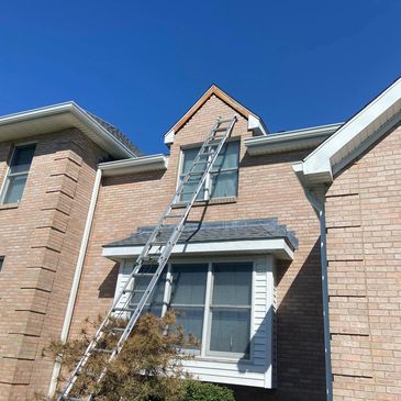 Tall ladder leaning against a brick house under clear blue sky.