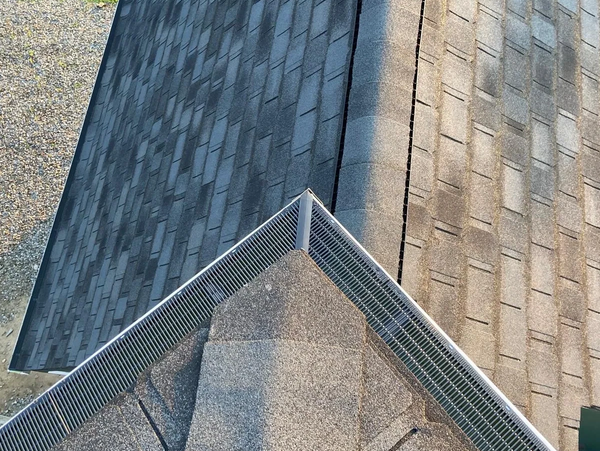 Overhead view of a roof intersection with different colored shingles and a metal gutter guard.