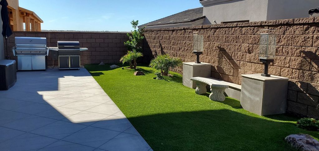 Backyard with grill, stone bench, and green lawn.