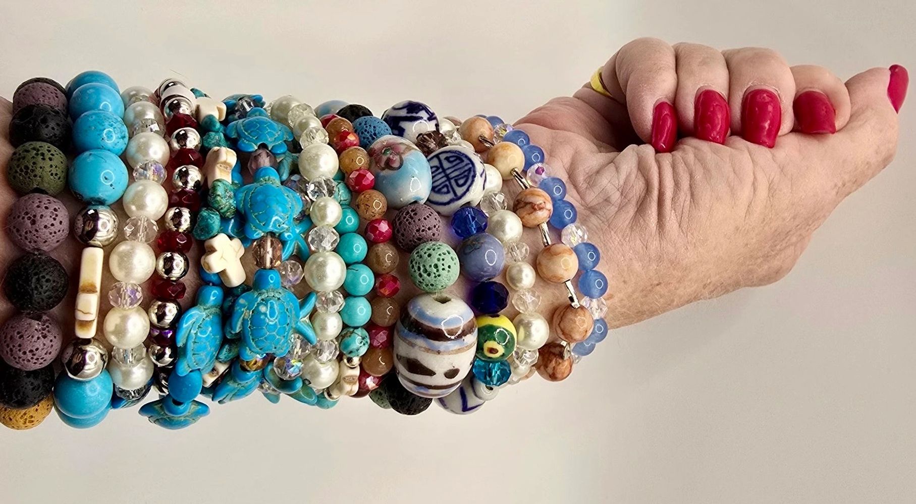 Arm adorned with multiple colorful beaded bracelets and red nail polish.