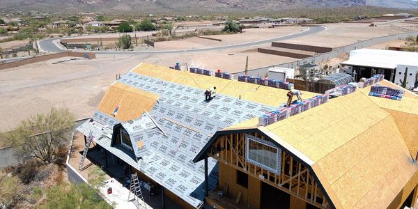 Workers installing roofing materials on a house under construction in a desert area.