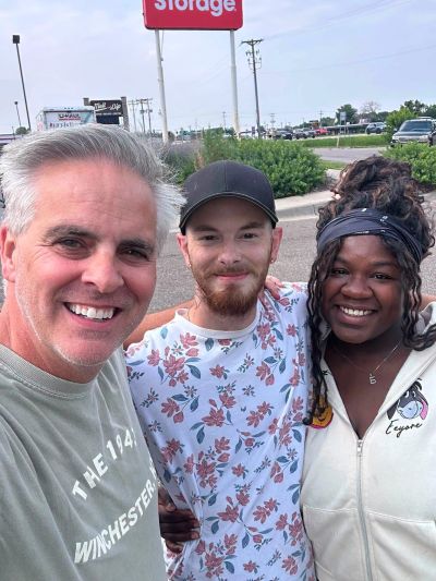 Three friends smiling outdoors in a parking lot.