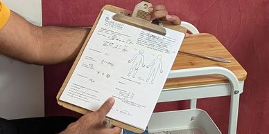 Person holding a medical assessment clipboard with a red wall and a small table in background.