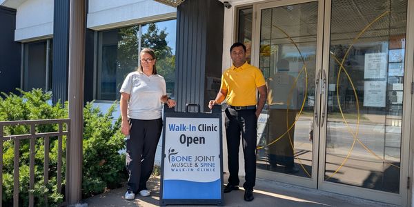 Two people standing outside a Bone Joint Muscle & Spine Walk-In Clinic with an open sign.