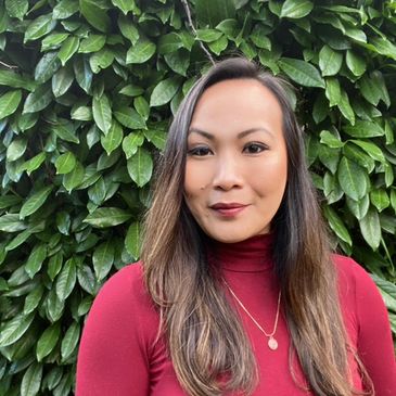 Woman in a red top posing in front of green leafy background.