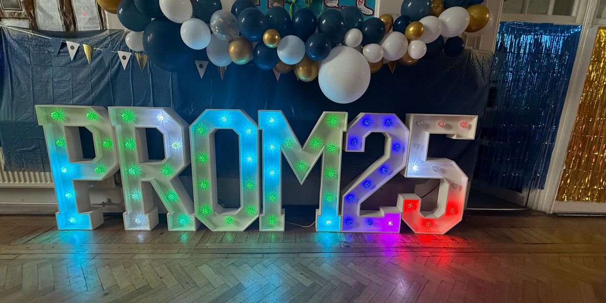 Illuminated PROM 25 sign with blue, white, and gold balloons above.