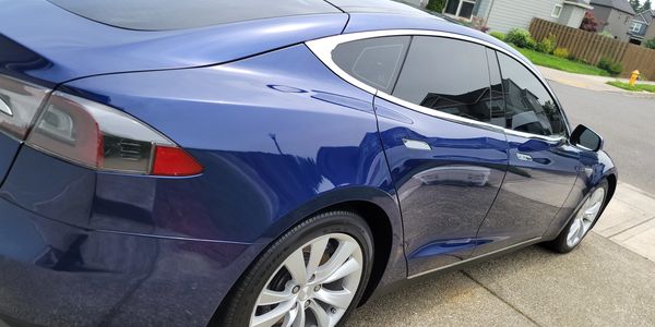Blue Tesla parked on the street beside a row of houses.