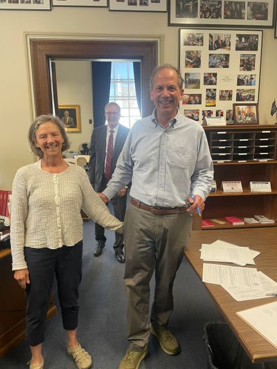 Three people smiling in an office, two holding hands, papers on desk.