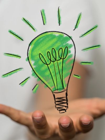 Hand holding a green light bulb illustration symbolizing eco-friendly ideas.