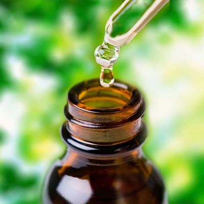 Dropper releasing liquid into brown bottle with green blurred background.