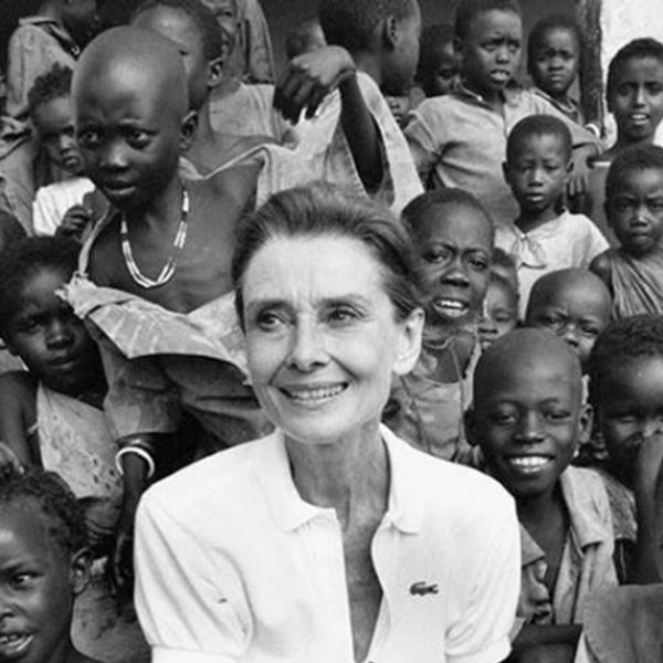 A woman smiling surrounded by a group of African children in a black-and-white photo.