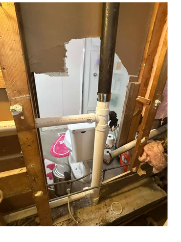 Exposed bathroom plumbing with a visible toilet and pipes behind a wall.