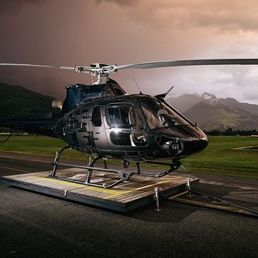 Black helicopter parked on helipad with mountains in the background.