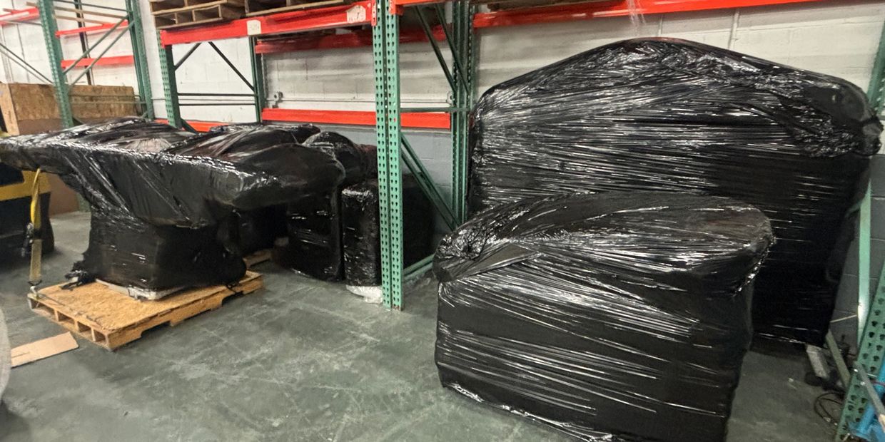 Large furniture pieces wrapped in black plastic in a warehouse.