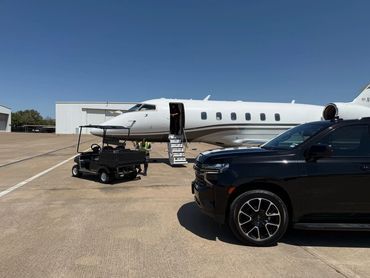 Private jet with open door on tarmac alongside black SUV and utility cart.