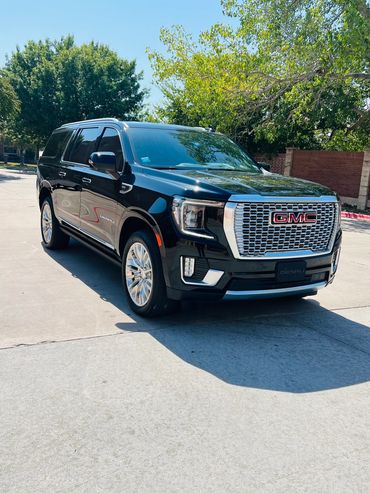 Black GMC Denali SUV parked on a sunny day with trees in the background.