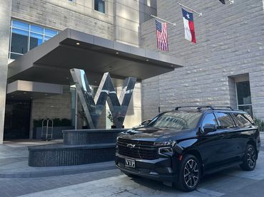 Black VIP SUV parked outside a modern building with a large metallic W sculpture.