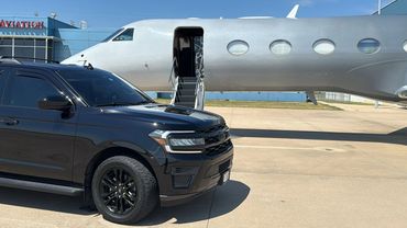 A black SUV parked near a private jet with an open door at an airport.