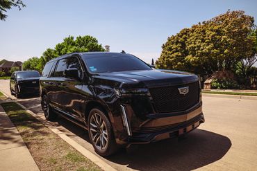 Two black Cadillac SUVs parked on a suburban street under a clear sky.