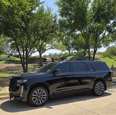 Black luxury SUV parked on a sunny street near a park with trees and a waterfall.