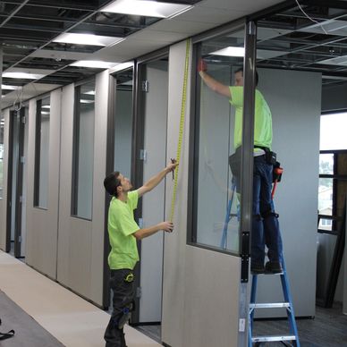 two men measuring a movable wall in office construction site