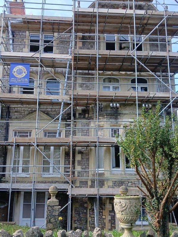 Stone building under renovation with scaffolding and a tree in front.