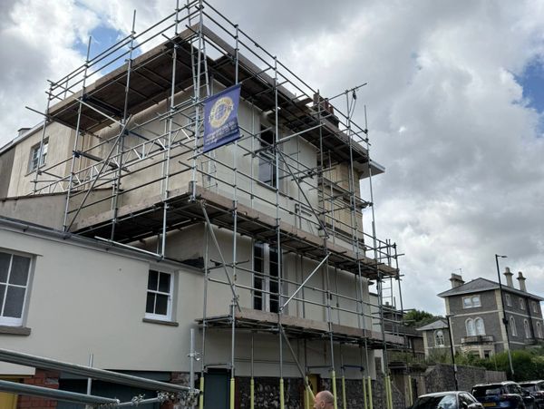 Three-story house covered in scaffolding for renovation on a cloudy day.