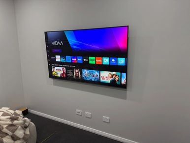 A modern TV mounted on a plain wall with streaming apps displayed.