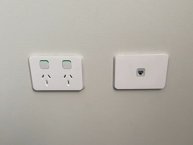 White power outlets and a network port on a light gray wall above dark carpet.