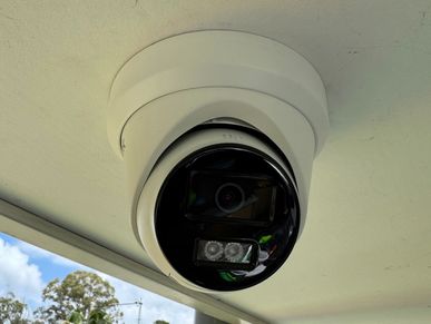 White security camera mounted on a ceiling outdoors.