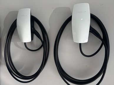 Two Tesla electric vehicle chargers mounted on a wall with coiled black cables.