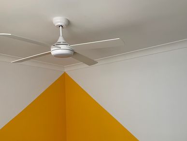 White ceiling fan above a corner with yellow and white painted walls.