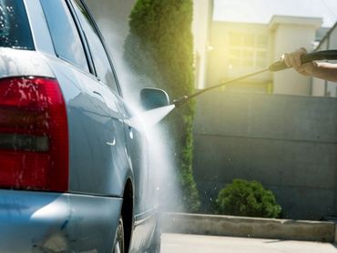 Worker in auto service is washing a luxury car by water hoses, backlight