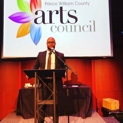 Darren Council speaking at a podium in front of the Prince William County Arts Council banner.