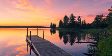 A serene wooden dock extends into a calm lake at sunset.