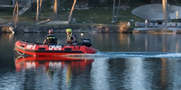 Two rescue workers on a red boat patrol a calm lake.