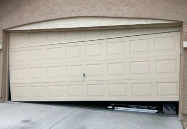 A garage door stuck halfway open with visible mechanical parts beneath.
